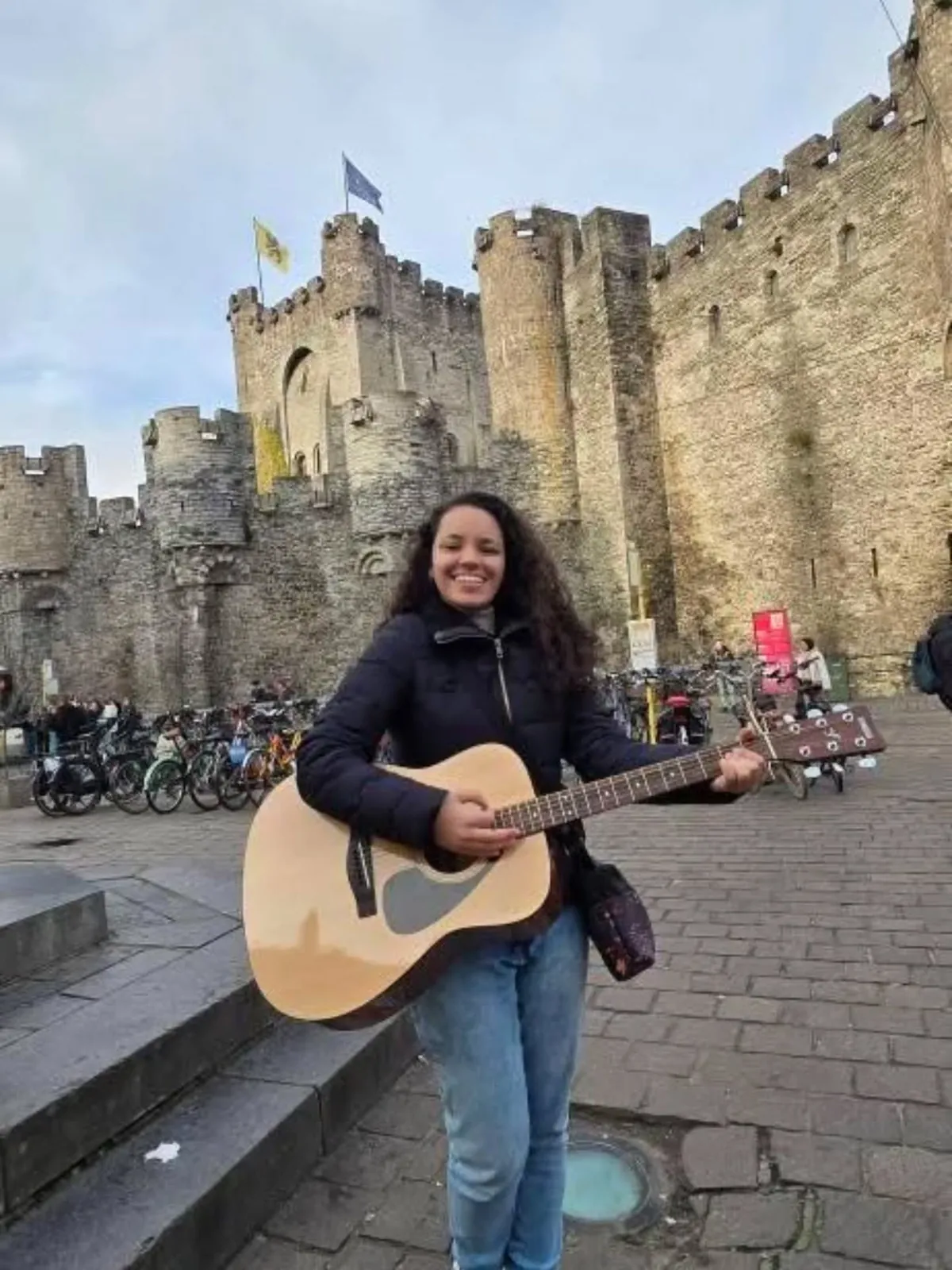 Victoria com violão em frente a um castelo medieval na Bélgica