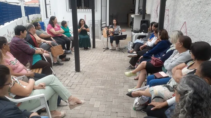 Roda musical com Victoria tocando violão para um grupo de mulheres